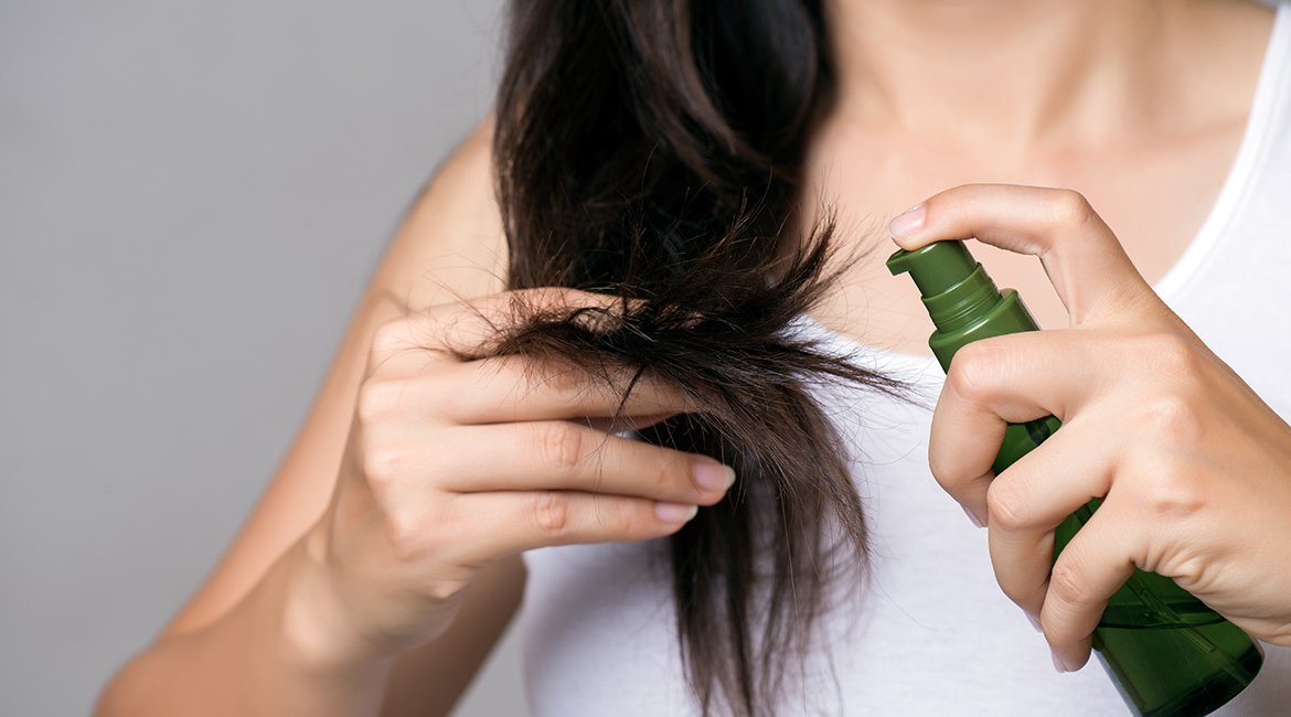 Junge Frau sprüht sich Haarpflege in ihre langen schwarzen Haare